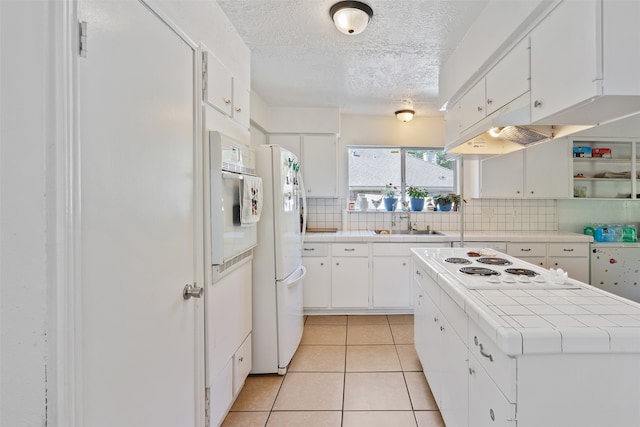 kitchen with tile countertops, decorative backsplash, white cabinets, and white appliances