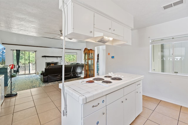 kitchen featuring tile countertops, light tile patterned flooring, a large fireplace, and white cabinets