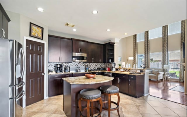 kitchen featuring decorative backsplash, a breakfast bar, stainless steel appliances, dark brown cabinetry, and a center island