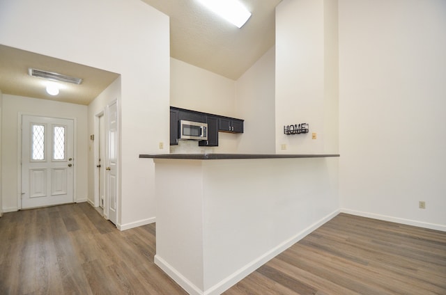 kitchen with kitchen peninsula, lofted ceiling, a textured ceiling, a kitchen bar, and dark wood-type flooring