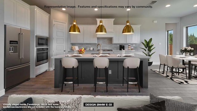 kitchen featuring pendant lighting, white cabinets, stainless steel appliances, and an island with sink