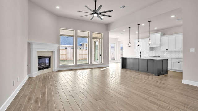 kitchen featuring visible vents, white cabinetry, open floor plan, light countertops, and an island with sink