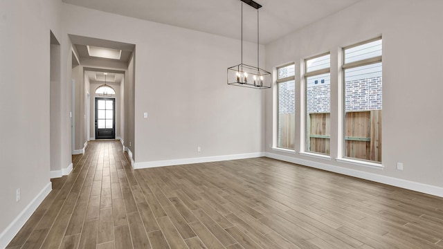 unfurnished dining area featuring a notable chandelier, baseboards, and wood finished floors