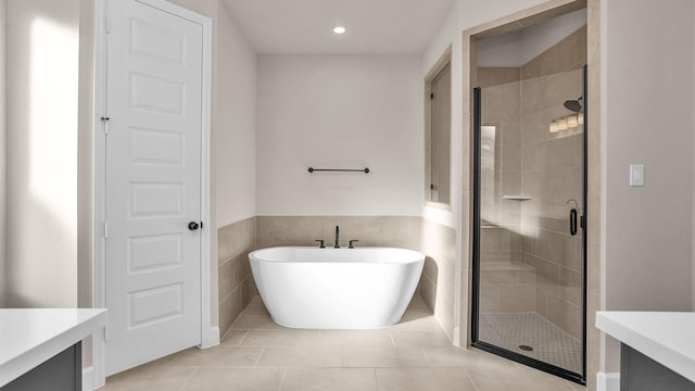 bathroom featuring tile walls, a soaking tub, a stall shower, vanity, and tile patterned flooring