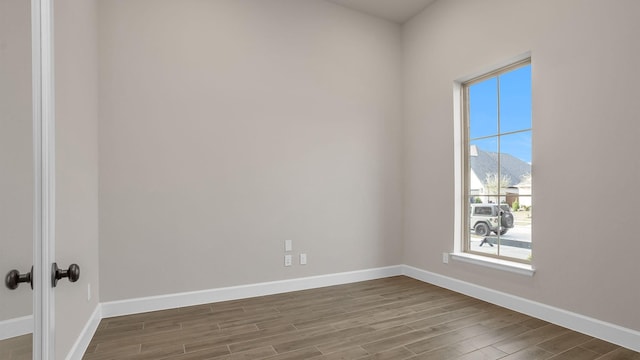 empty room with wood finished floors, a mountain view, and baseboards