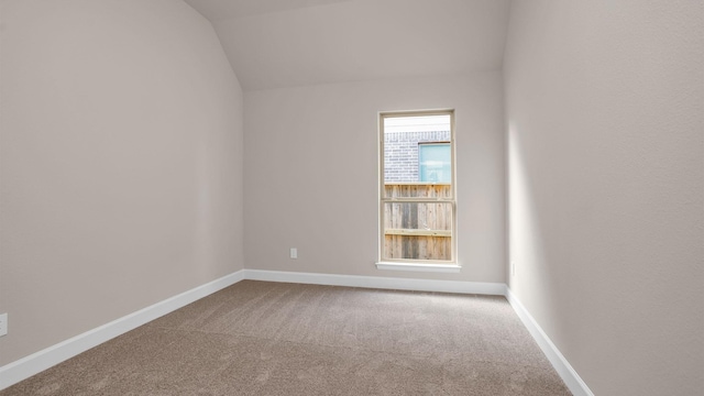 carpeted spare room with vaulted ceiling and baseboards