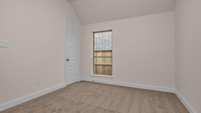 spare room featuring lofted ceiling, baseboards, and light colored carpet