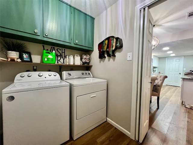 clothes washing area with cabinets, washing machine and clothes dryer, and light hardwood / wood-style flooring