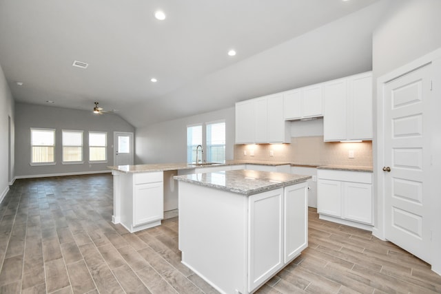 kitchen with lofted ceiling, a kitchen island, light hardwood / wood-style flooring, kitchen peninsula, and white cabinets