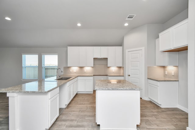 kitchen featuring lofted ceiling, light hardwood / wood-style flooring, sink, a center island, and white cabinets