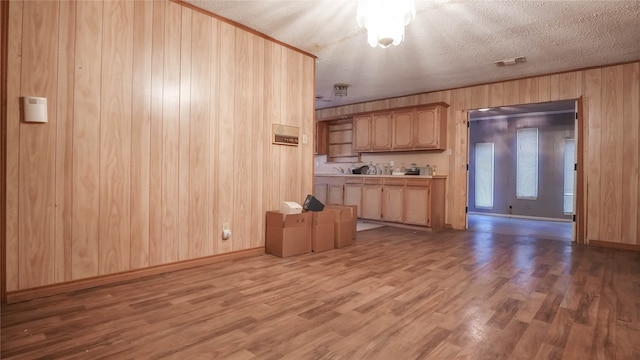 kitchen with light hardwood / wood-style flooring, a textured ceiling, wooden walls, and light brown cabinetry