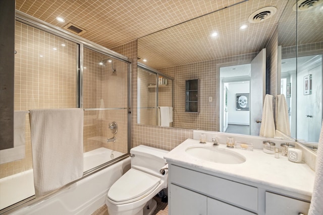 full bathroom featuring vanity, toilet, tile walls, and bath / shower combo with glass door