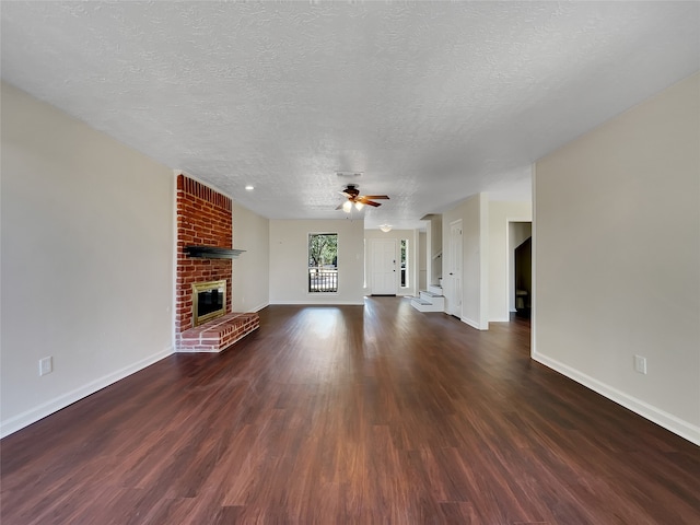 unfurnished living room with dark hardwood / wood-style floors, ceiling fan, a textured ceiling, and a brick fireplace