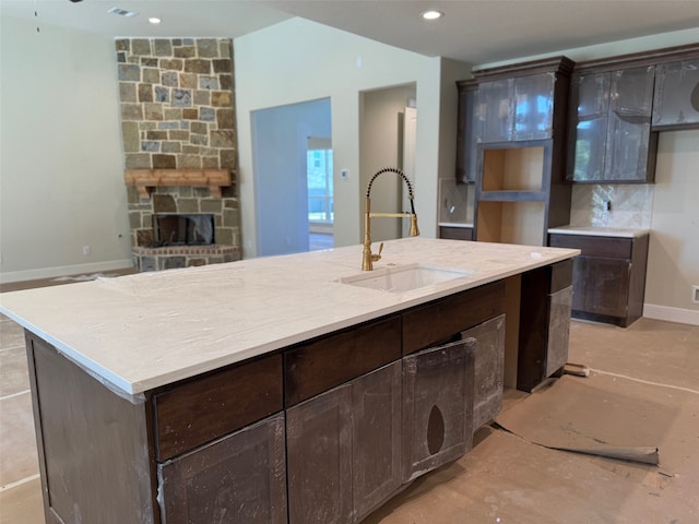 kitchen with dark brown cabinets, a fireplace, sink, and an island with sink