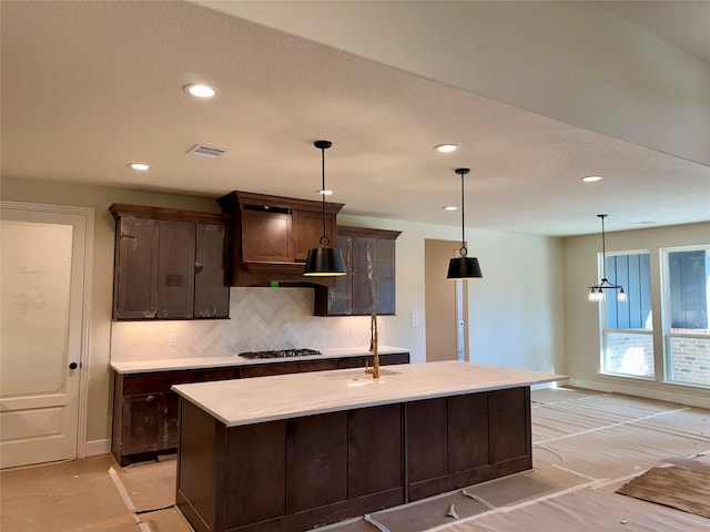 kitchen featuring sink, hanging light fixtures, a chandelier, dark brown cabinets, and a center island with sink