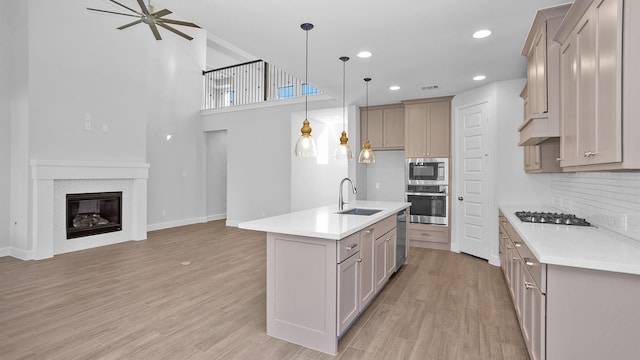 kitchen with pendant lighting, stainless steel appliances, an island with sink, sink, and light wood-type flooring