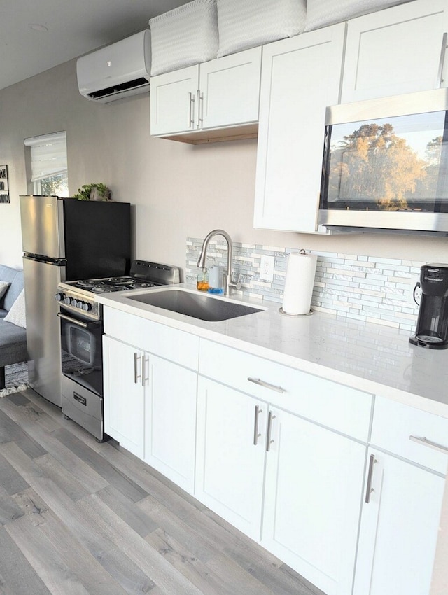 kitchen with a wall mounted AC, appliances with stainless steel finishes, white cabinetry, light hardwood / wood-style floors, and sink