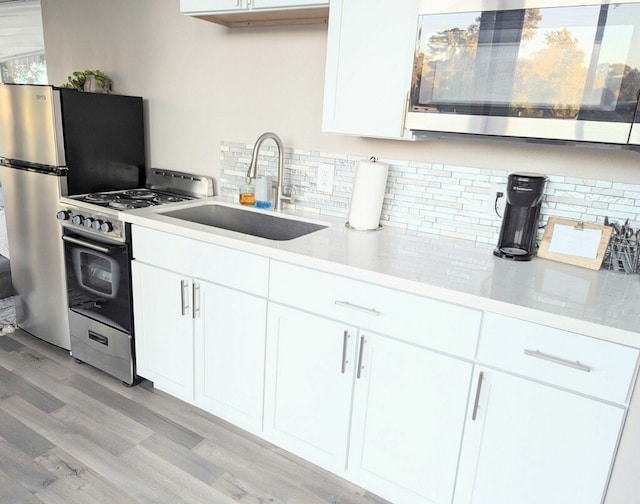 kitchen with tasteful backsplash, white cabinetry, light hardwood / wood-style flooring, sink, and stainless steel appliances