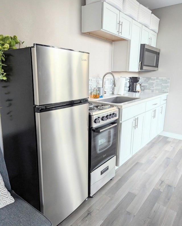 kitchen with appliances with stainless steel finishes, white cabinetry, sink, and backsplash