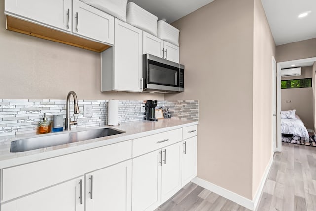 kitchen featuring sink, a wall mounted air conditioner, backsplash, white cabinets, and light hardwood / wood-style flooring