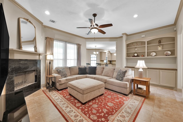 living room featuring a high end fireplace, ornamental molding, ceiling fan with notable chandelier, built in features, and light tile patterned flooring