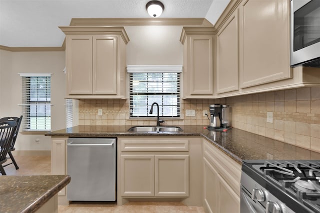 kitchen featuring ornamental molding, stainless steel appliances, sink, cream cabinets, and dark stone countertops