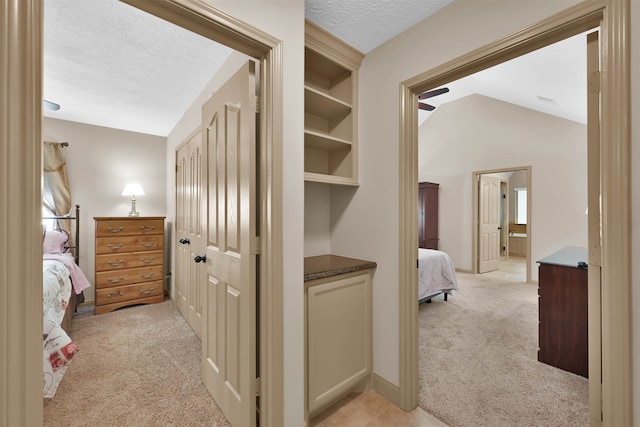 hallway featuring a textured ceiling, light carpet, and vaulted ceiling