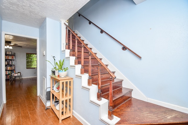 staircase with hardwood / wood-style floors, a textured ceiling, and ceiling fan