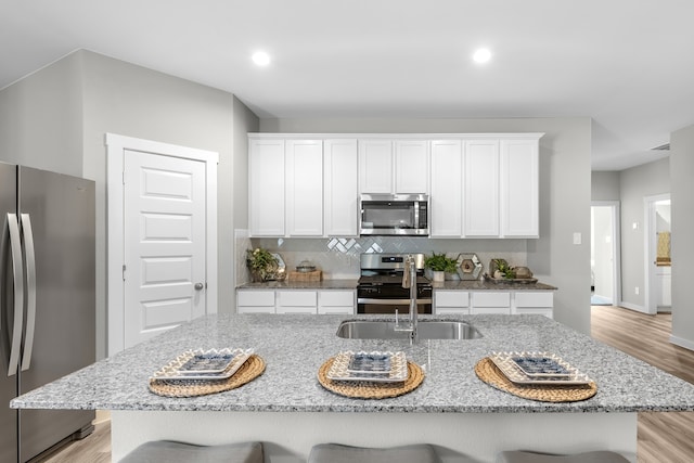 kitchen with appliances with stainless steel finishes, a kitchen breakfast bar, white cabinets, light hardwood / wood-style flooring, and a center island with sink