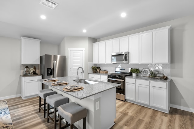 kitchen featuring appliances with stainless steel finishes, white cabinetry, a kitchen island with sink, light hardwood / wood-style flooring, and sink