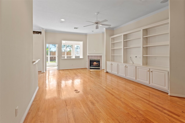 unfurnished living room with a tiled fireplace, light hardwood / wood-style flooring, ornamental molding, built in shelves, and ceiling fan