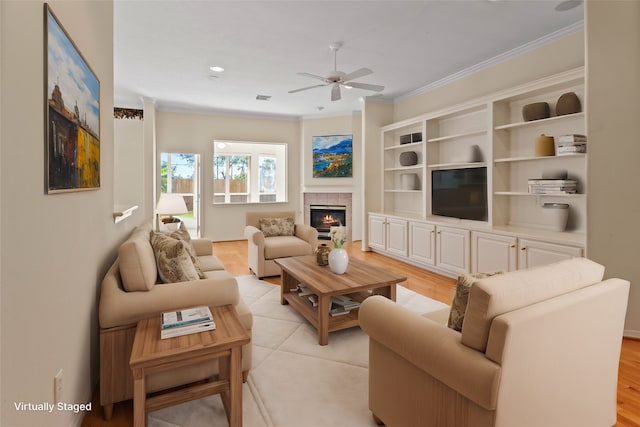 living room featuring light hardwood / wood-style floors, ornamental molding, a tiled fireplace, and ceiling fan