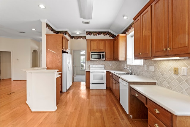 kitchen with white appliances, a sink, light wood-type flooring, brown cabinetry, and crown molding