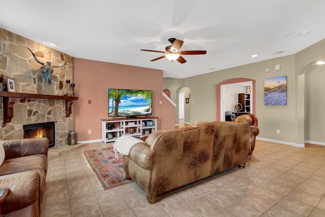 tiled living room featuring a stone fireplace and ceiling fan