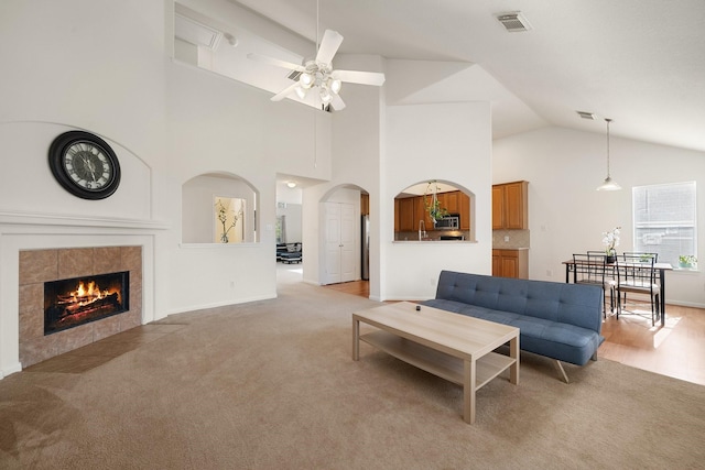 living room featuring a fireplace, light colored carpet, high vaulted ceiling, and ceiling fan