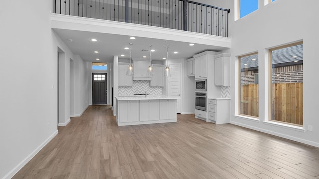 kitchen with stainless steel oven, decorative light fixtures, light hardwood / wood-style flooring, a center island, and white cabinetry