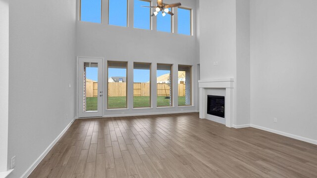 unfurnished living room with ceiling fan, wood-type flooring, a towering ceiling, and a wealth of natural light