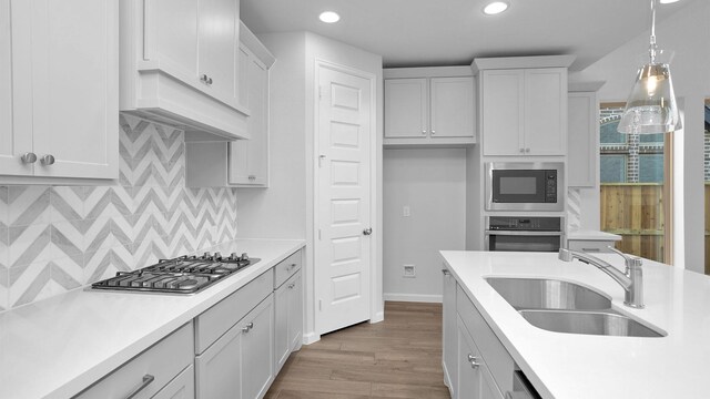 kitchen with pendant lighting, white cabinets, sink, hardwood / wood-style flooring, and stainless steel appliances