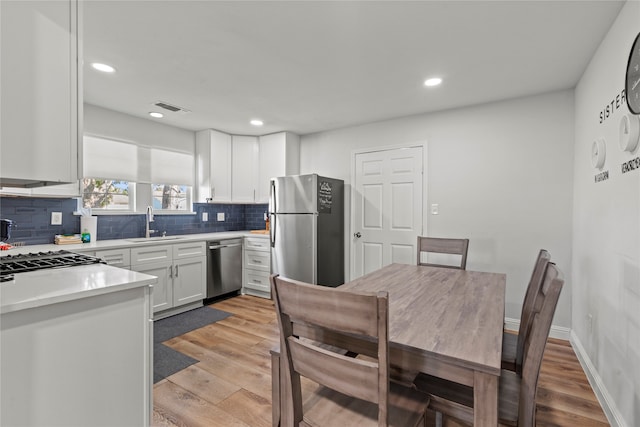 kitchen featuring stainless steel appliances, backsplash, sink, light wood-type flooring, and white cabinetry