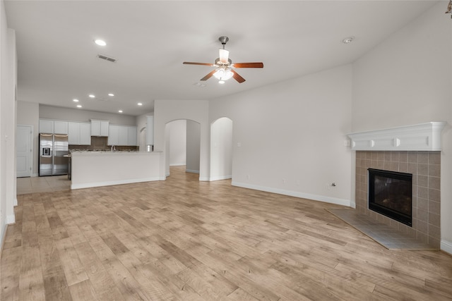 unfurnished living room featuring light hardwood / wood-style flooring, a tiled fireplace, and ceiling fan