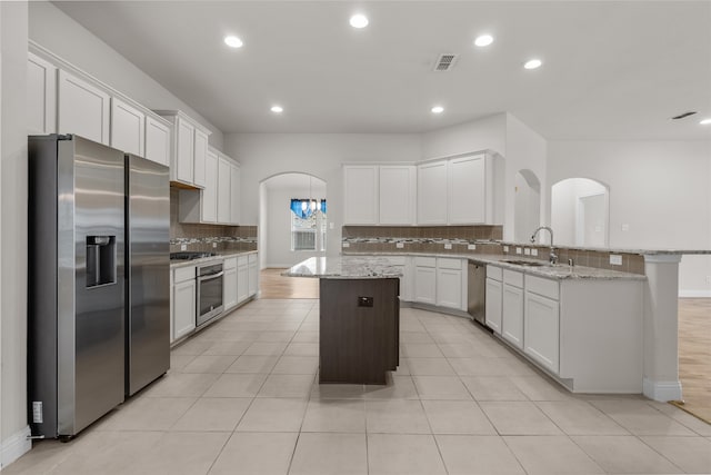 kitchen featuring white cabinets, light stone counters, a kitchen island, sink, and stainless steel appliances