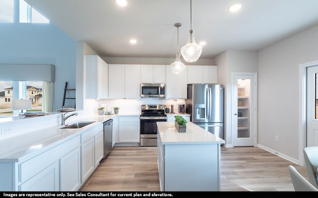 kitchen featuring hanging light fixtures, light stone counters, appliances with stainless steel finishes, white cabinetry, and sink