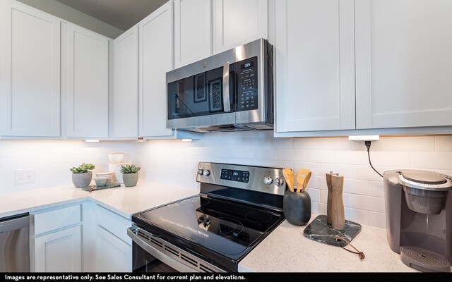 kitchen featuring appliances with stainless steel finishes, white cabinetry, light stone counters, and backsplash