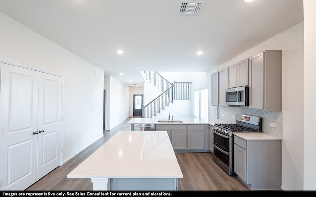 kitchen with hardwood / wood-style flooring, kitchen peninsula, stainless steel appliances, sink, and gray cabinets