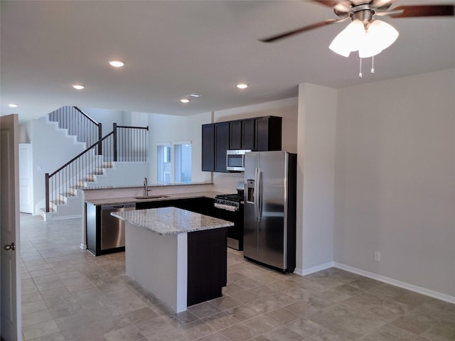 kitchen featuring a kitchen island, sink, ceiling fan, light stone counters, and stainless steel appliances