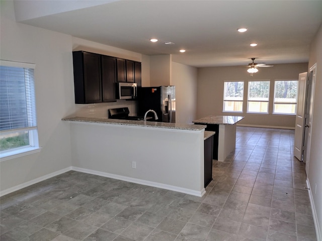 kitchen featuring light stone counters, tasteful backsplash, kitchen peninsula, ceiling fan, and stainless steel appliances