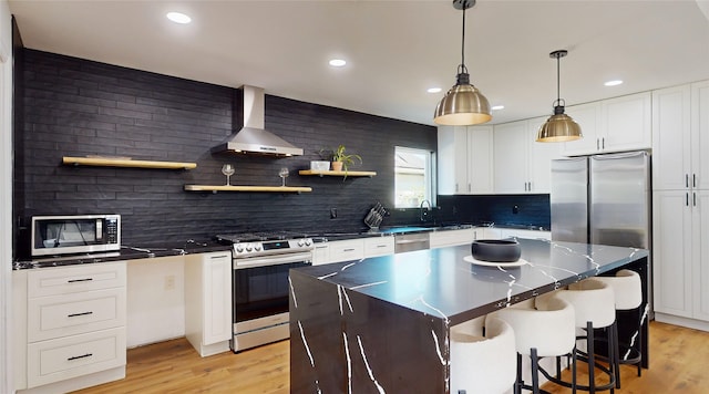 kitchen with stainless steel appliances, wall chimney exhaust hood, light wood-type flooring, and a kitchen island