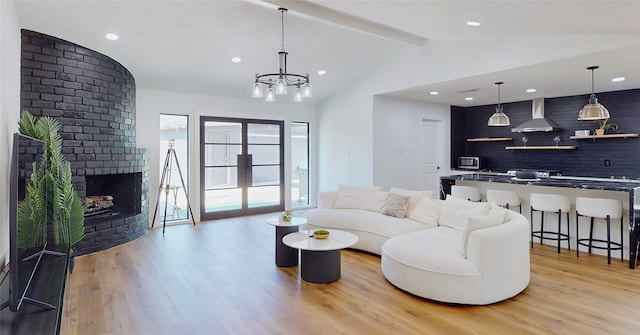 living room featuring a notable chandelier, lofted ceiling with beams, light wood-type flooring, and a fireplace