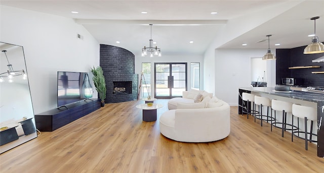 living room with light hardwood / wood-style flooring, vaulted ceiling with beams, an inviting chandelier, and a brick fireplace