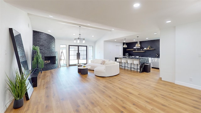 living room with light hardwood / wood-style flooring, an inviting chandelier, lofted ceiling, and a fireplace